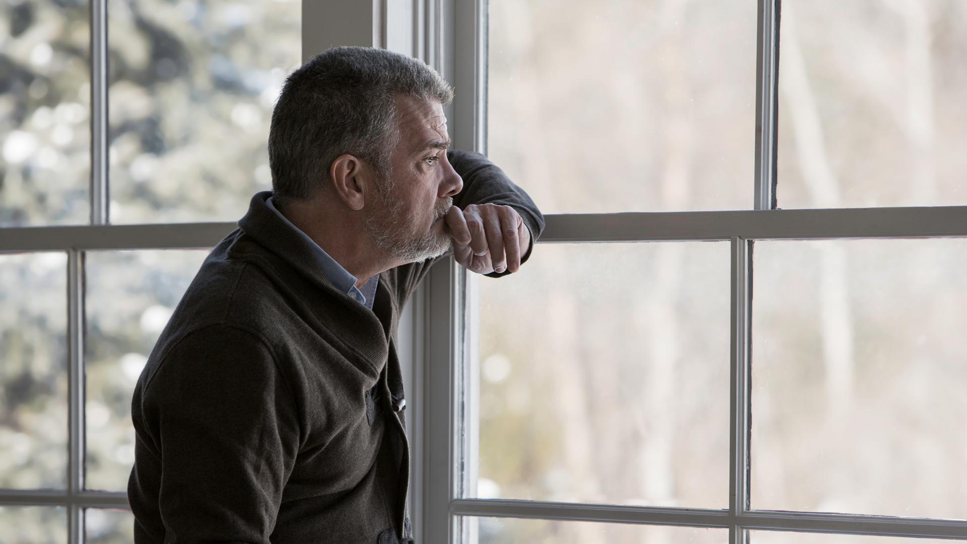 Elderly person sitting alone on a sofa, looking down with a sad expression, illustrating symptoms of depression in older adults.