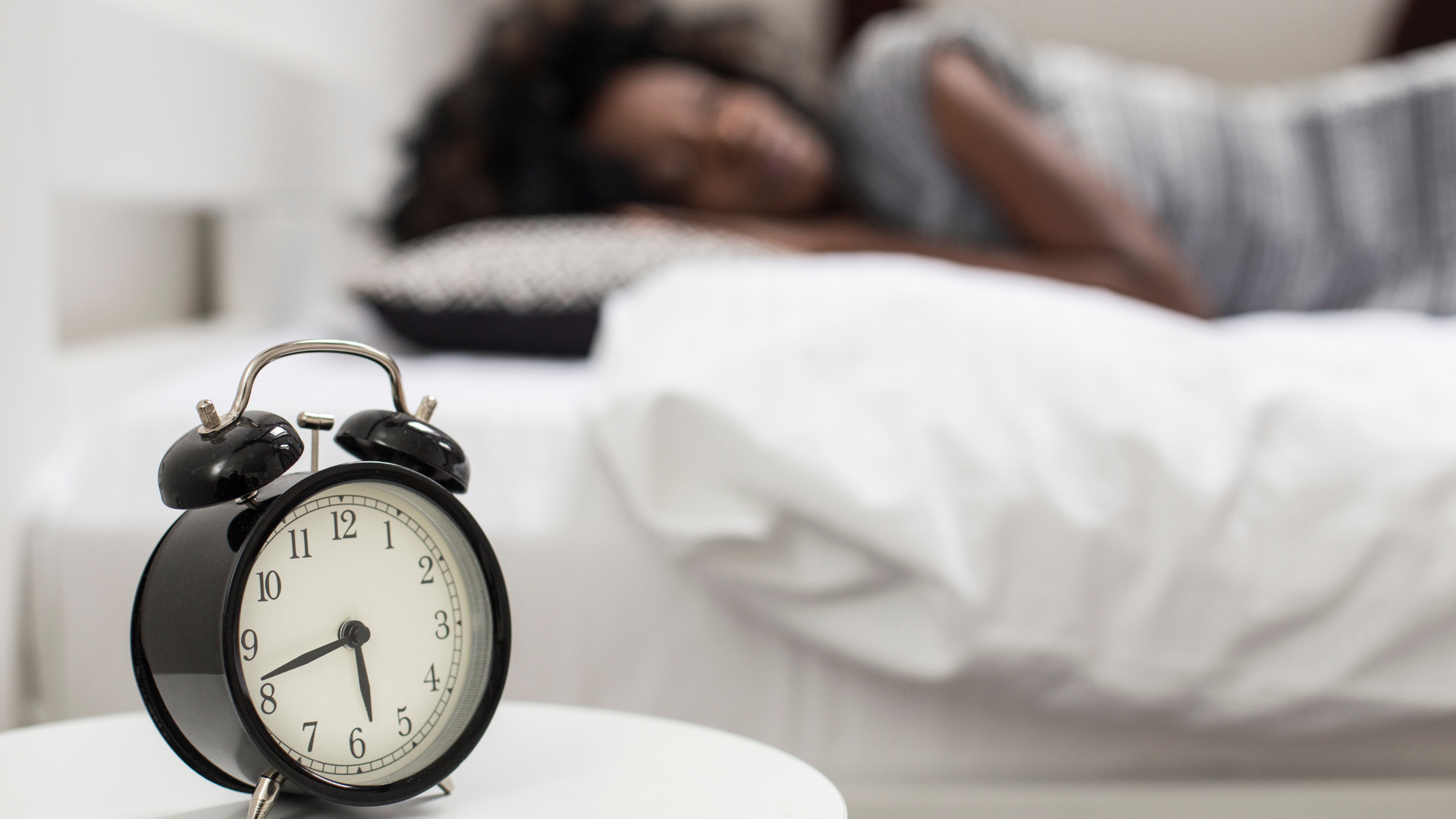 Person adjusting alarm clock on bedside table at night, aiming to fix their sleep schedule for better rest and improved daily routine.