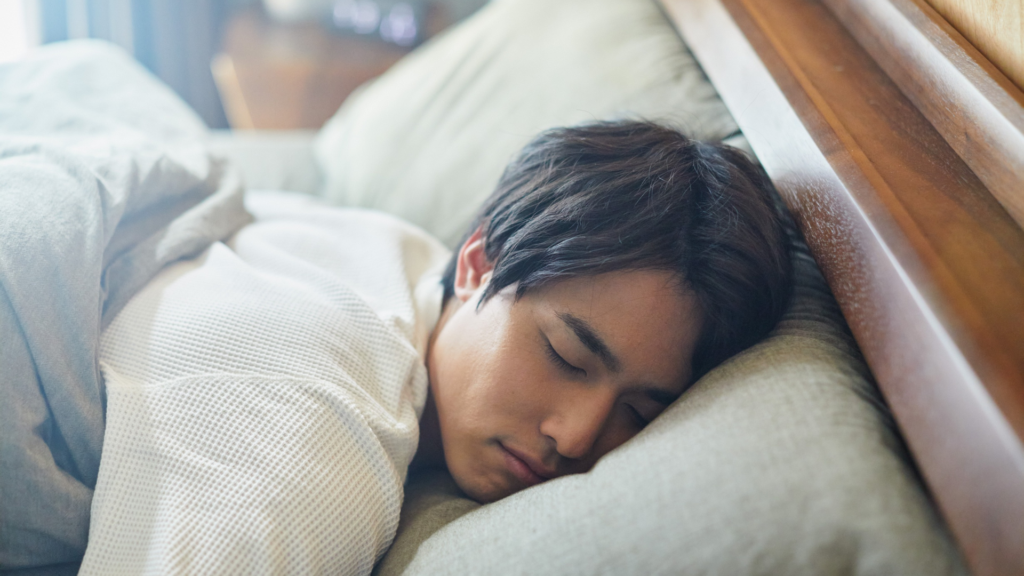 A person sleeping peacefully in a dark, quiet bedroom with blackout curtains and a white noise machine, illustrating how to stay asleep all night.