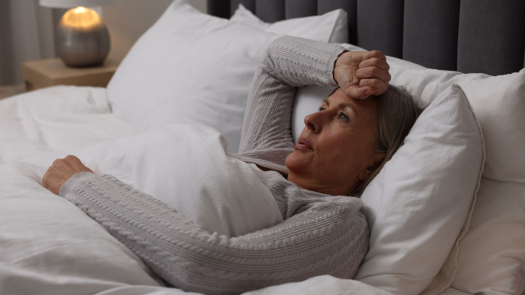 Middle-aged woman lying awake in bed at night, looking frustrated, illustrating insomnia commonly experienced during menopause.