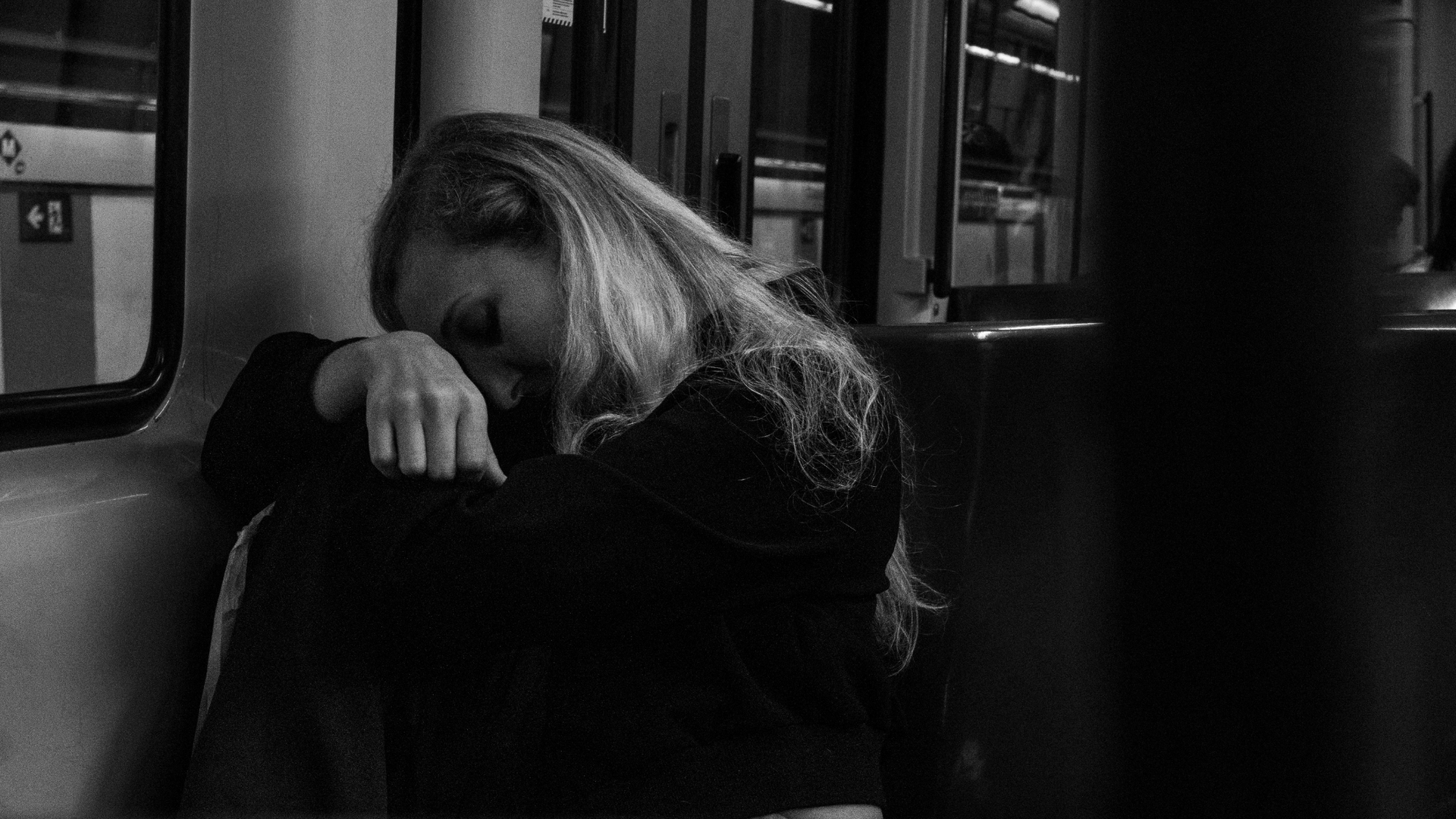 A solitary figure sits by a rain-streaked window, gazing outside with a distant, melancholic expression, evoking a sense of quiet sadness and reflection.