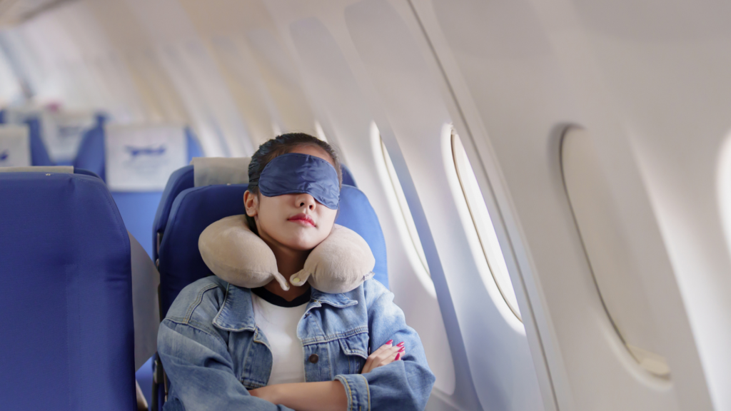 Passenger uses a travel pillow and eye mask while reclining in an airplane seat, demonstrating tips for sleeping comfortably on a plane during a flight.