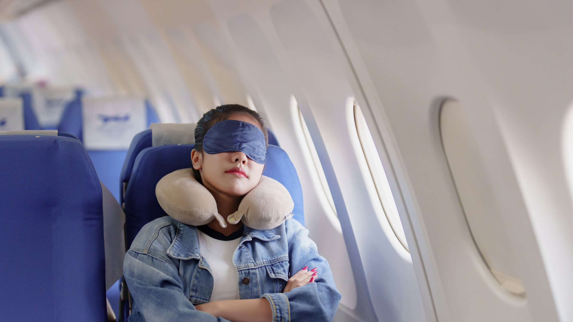 Passenger uses a travel pillow and eye mask while reclining in an airplane seat, demonstrating tips for sleeping comfortably on a plane during a flight.