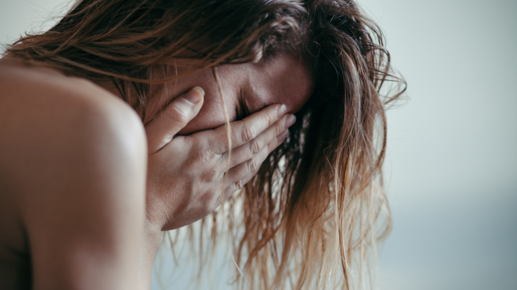 A person sits alone in a dimly lit room, holding their head in their hands, overwhelmed by intense emotional pain and distress.