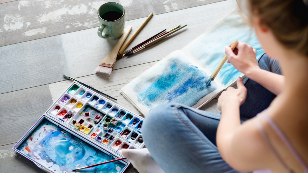 A group of people engaging in art therapy activities, painting and drawing together in a bright, supportive studio environment to promote emotional healing.
