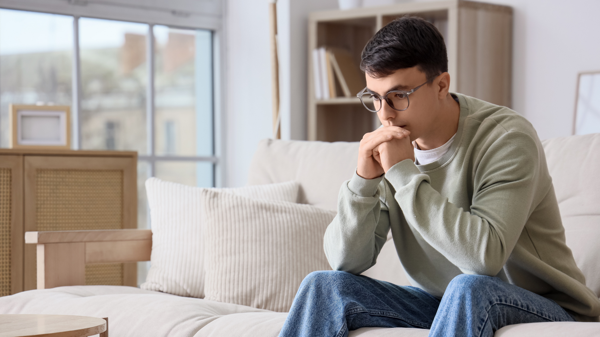A person sits alone with slumped shoulders, head down, surrounded by taller confident figures, visually representing feelings of inferiority and self-doubt.