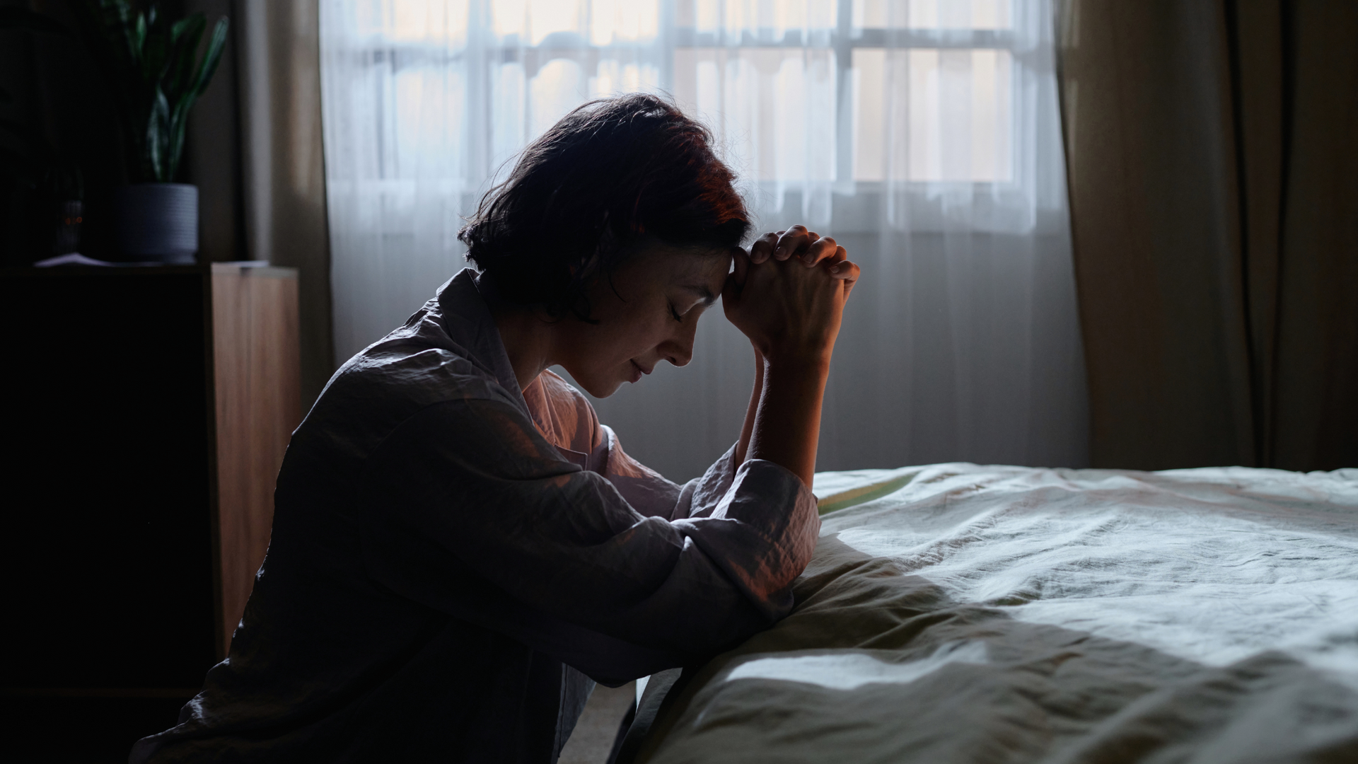 A person sitting quietly with hands clasped in prayer, seeking comfort and strength for mental health and emotional well-being in a peaceful setting.
