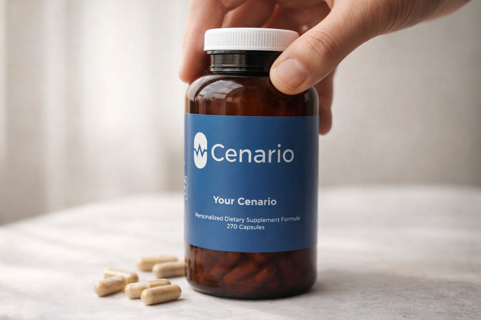 Hand holding supplement bottle labeled Cenario with capsules beside it
