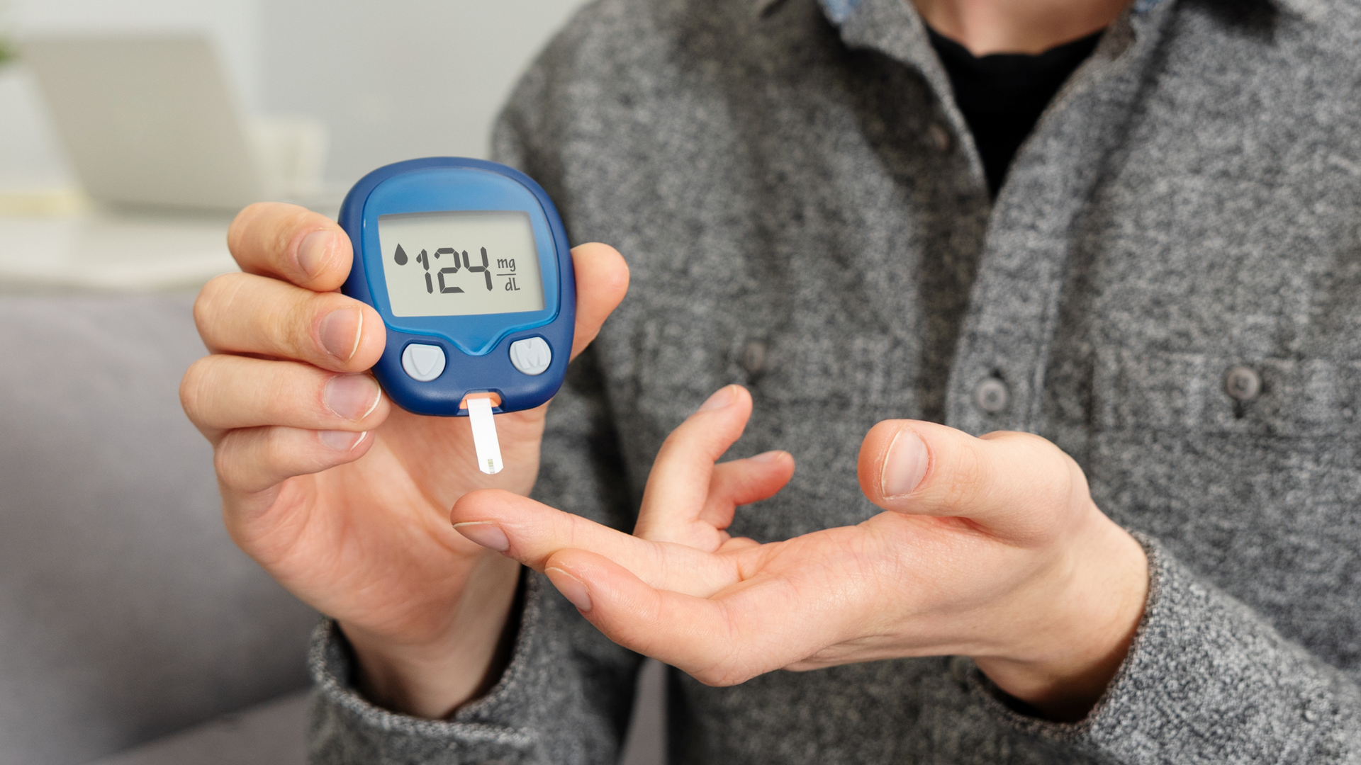 A digital glucometer displaying a blood sugar reading, with a test strip inserted and a drop of blood on the sensor, used for diabetes monitoring.