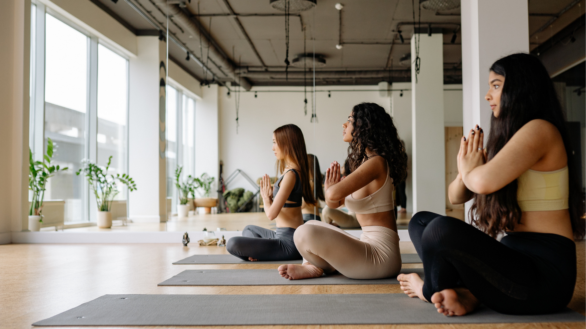 A person sitting cross-legged on a yoga mat with eyes closed, practicing guided meditation in a peaceful, softly lit indoor space.